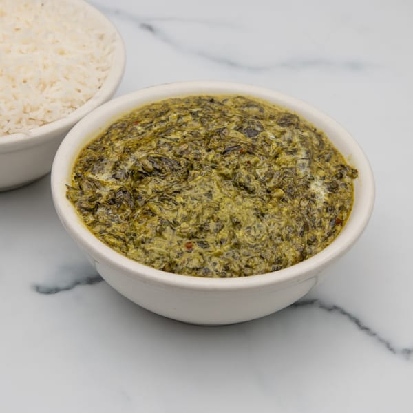 A bowl of vibrant green Indian palak paneer, with a bowl of white rice in the background.
