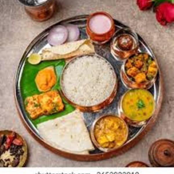A traditional Indian thali meal with rice, curries, flatbread, and drinks on a silver platter.