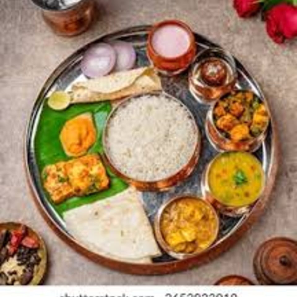 A traditional Indian thali meal with rice, curries, flatbread, and drinks on a silver platter.
