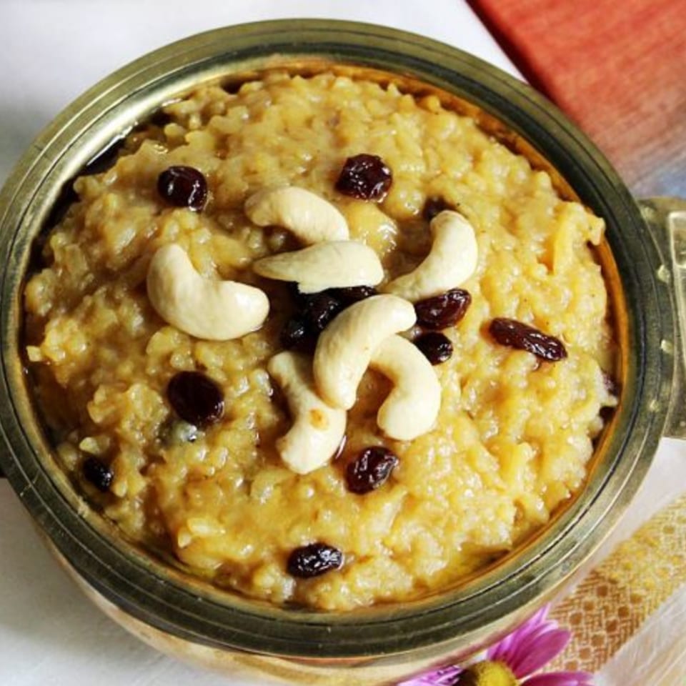 Sweet pongal, a South Indian rice dish, garnished with cashews and raisins in a brass bowl.