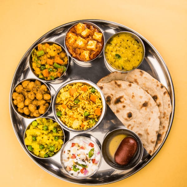 A traditional Indian thali with various dishes, including paneer, dal, vegetables, rice, roti, and dessert.