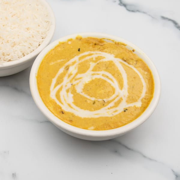 A bowl of creamy Indian curry with a swirl of white sauce, next to a bowl of white rice.