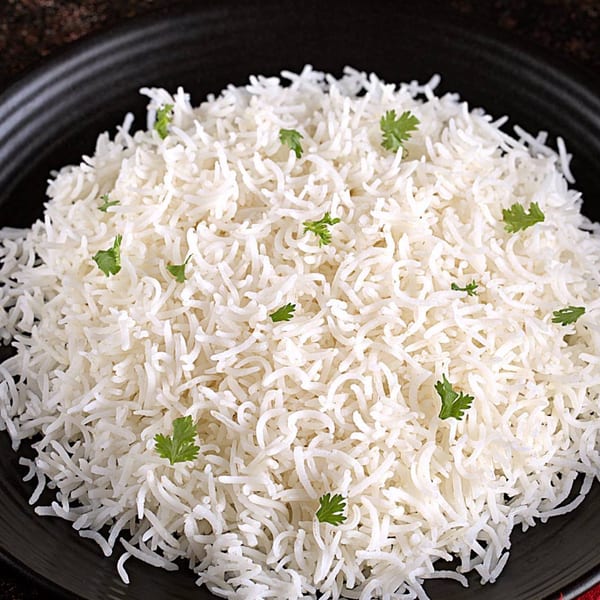 Fluffy white basmati rice, garnished with fresh green cilantro, served on a dark plate.