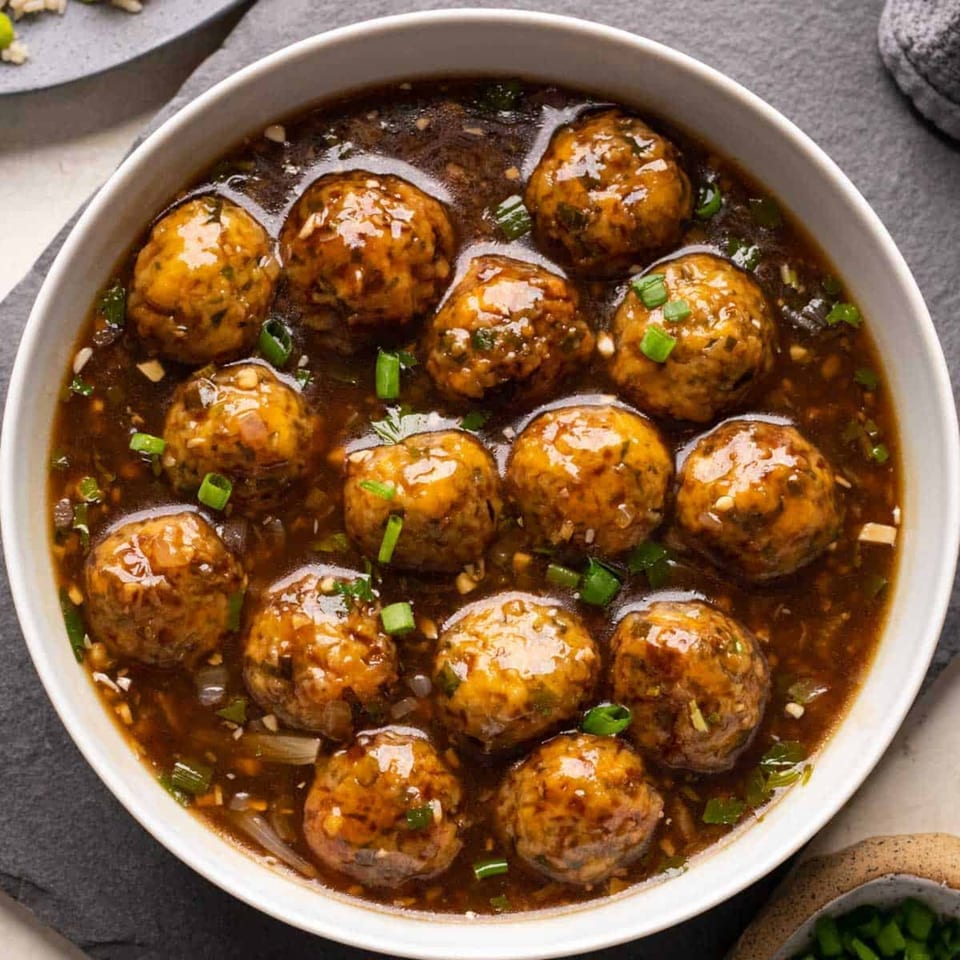 A white bowl filled with Manchurian vegetable balls in a rich brown gravy, garnished with green onions.