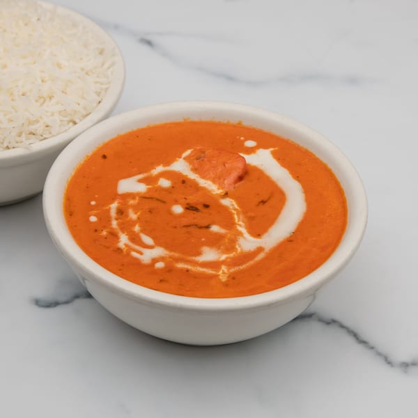 A bowl of vibrant orange Indian butter chicken with a swirl of cream, next to white rice.