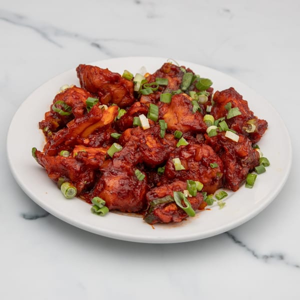 Mintt Indian Cuisine's chili chicken, a vibrant red dish garnished with fresh green onions on a white plate.