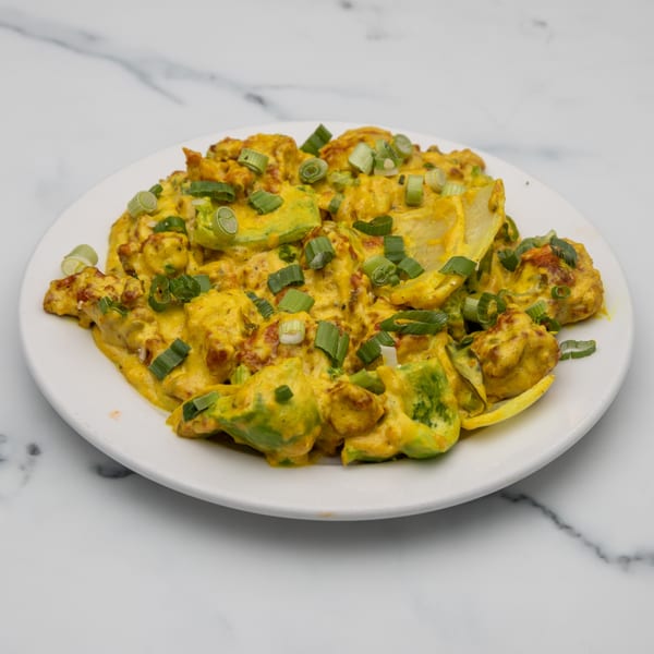 Mintt Indian Cuisine's yellow curry dish with avocado chunks and green onions on a white plate.