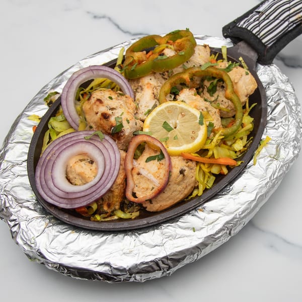 Indian chicken tikka sizzler with onions, bell peppers, and lemon, served on a hot plate.