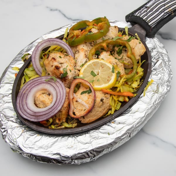 Mintt Indian Cuisine's chicken tikka sizzler with onions, peppers, and lemon on a hot plate.