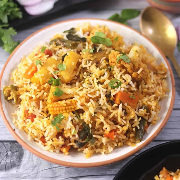 A close-up of vegetable biryani with rice, carrots, baby corn, and green beans, garnished with cilantro.