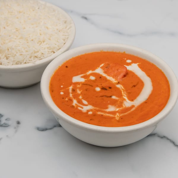 A bowl of creamy orange butter chicken with a swirl of white cream, next to a bowl of white rice.