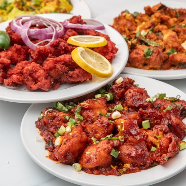 Three plates of vibrant red Indian chicken dishes, garnished with onions, lemons, and green herbs.