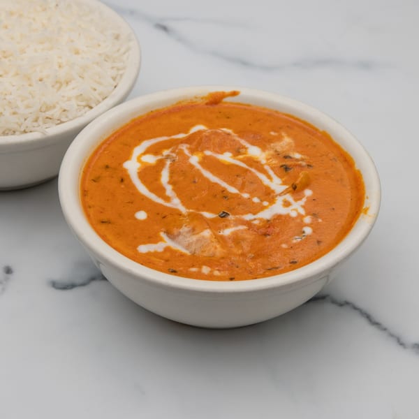 A bowl of creamy orange Indian curry with white swirls, next to a bowl of white rice.
