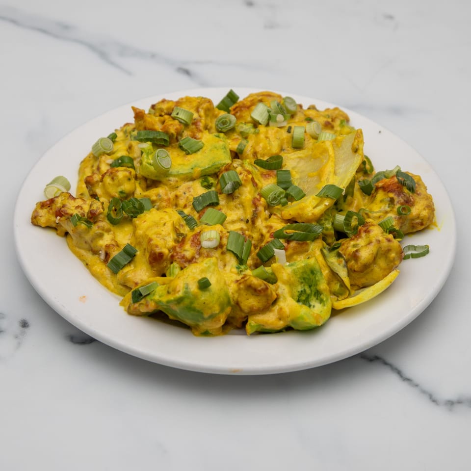 A plate of Indian food with yellow curry, avocado, and green onions on a white marble surface.