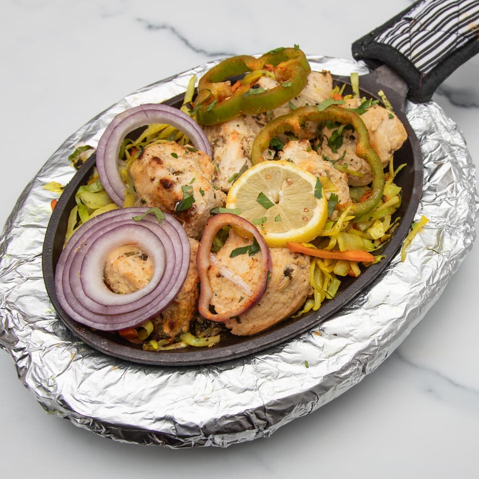 Indian chicken tikka sizzler with onions, bell peppers, and lemon, served on a hot plate.