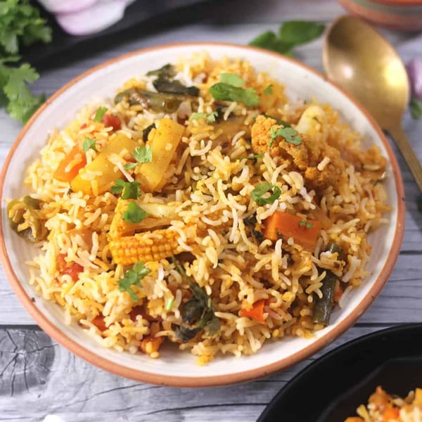 A close-up of a white bowl filled with vegetable biryani, garnished with fresh cilantro.