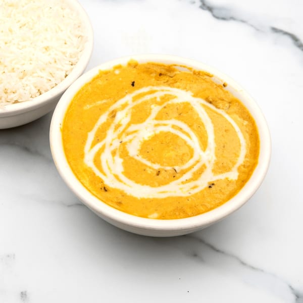 A bowl of creamy orange Indian curry with a swirl of white cream, next to a bowl of white rice.