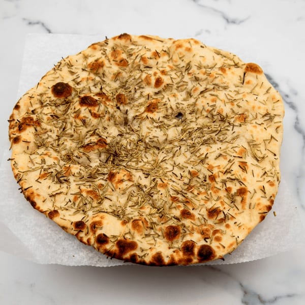 Round Indian flatbread, likely naan, topped with dried rosemary, on white parchment paper.