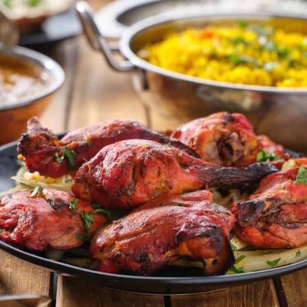 A plate of tandoori chicken drumsticks with onions, cilantro, and a bowl of yellow rice.