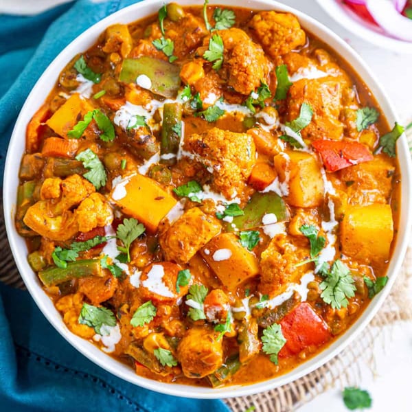 A vibrant vegetable curry with cauliflower, peppers, and potatoes, garnished with cilantro and cream swirls.
