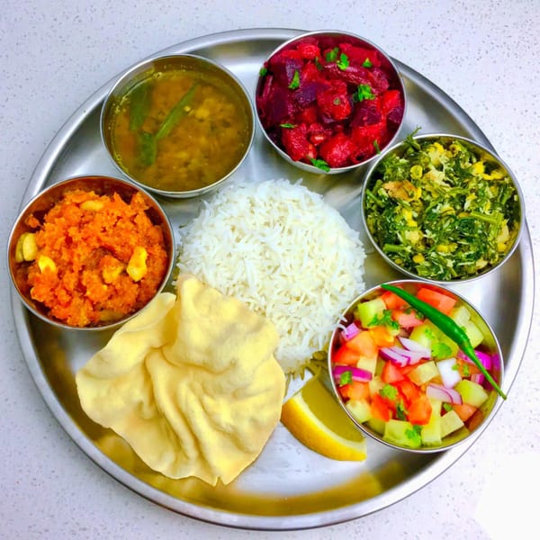 A vibrant Indian thali with rice, dal, beet curry, greens, carrot halwa, salad, and papad.