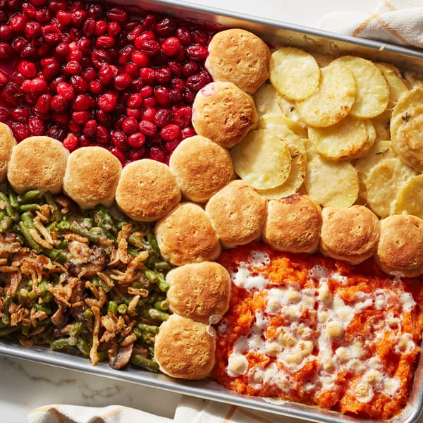 A baking sheet filled with cranberry sauce, scalloped potatoes, green bean casserole, sweet potato casserole, and biscuits.