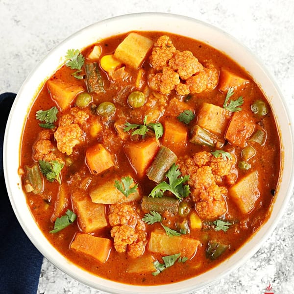 Close-up of a vibrant vegetable curry with cauliflower, potatoes, and green beans, garnished with cilantro.