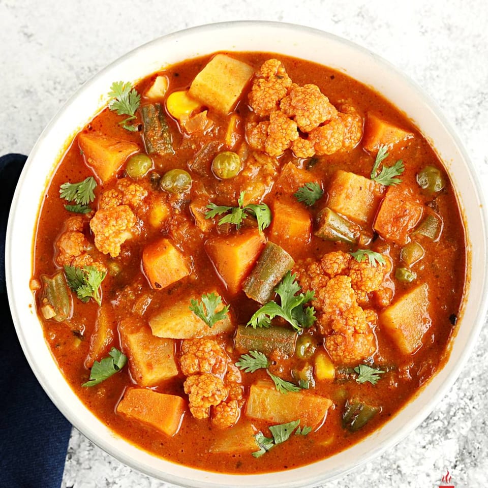 Close-up of a vibrant vegetable curry with cauliflower, potatoes, and green beans, garnished with cilantro.